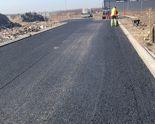 Ipari út gépi aszfaltozása munkásokkal, szegélykővel és billenccsel