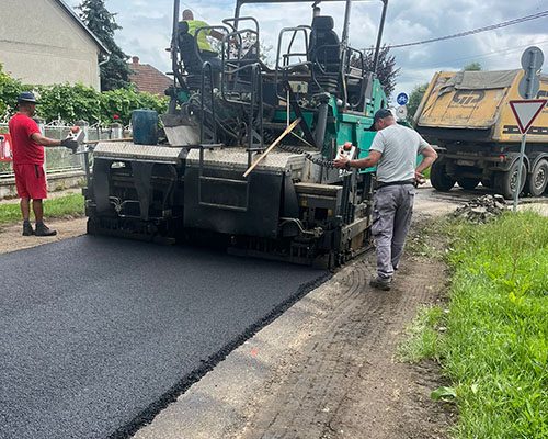 Aszfaltfiniser kopóréteget terít lakóutcában, billencsből adagolva
