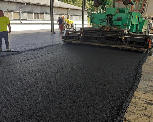Aszfaltfiniser kopóréteget terít fedett csarnok alatt